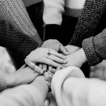 black and white image of a group of hands stacked on top of each other in the center of a huddle